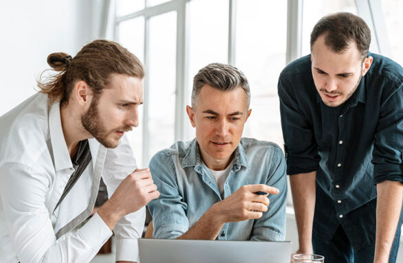 Three men collaborating intently over a laptop in a bright office. Three men collaborating intently over a laptop in a bright office.
