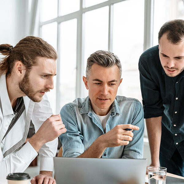 Three men collaborating intently over a laptop in a bright office. Three men collaborating intently over a laptop in a bright office.
