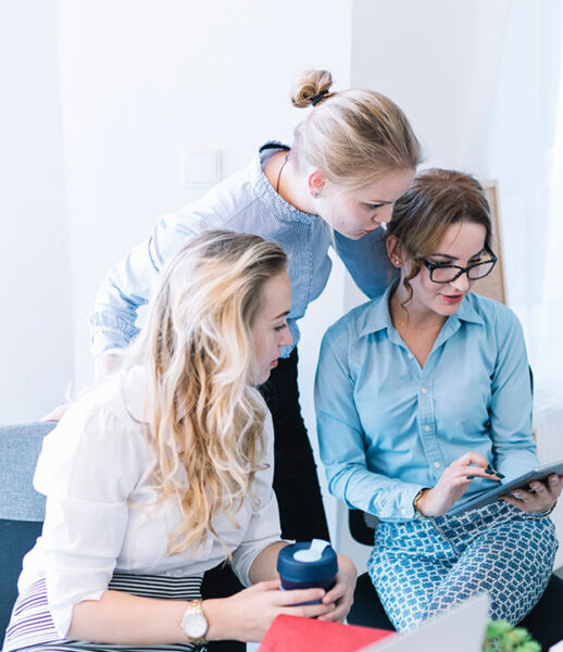 Three women collaborating and looking at a tablet in a bright office. Three women collaborating and looking at a tablet in a bright office.