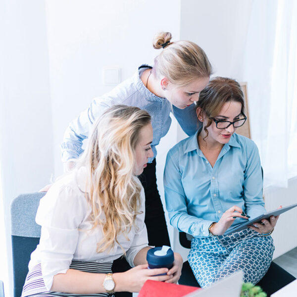 Three women collaborating and looking at a tablet in a bright office. Three women collaborating and looking at a tablet in a bright office.