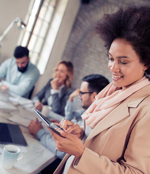 Smiling woman using a tablet in a busy office with colleagues working in the background. Smiling woman using a tablet in a busy office with colleagues working in the background.