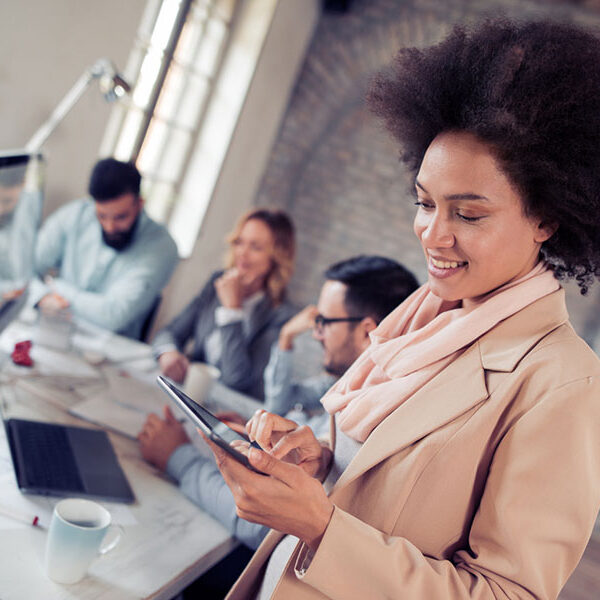 Smiling woman using a tablet in a busy office with colleagues working in the background. Smiling woman using a tablet in a busy office with colleagues working in the background.