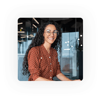 Smiling woman with curly hair and glasses in a modern office setting.